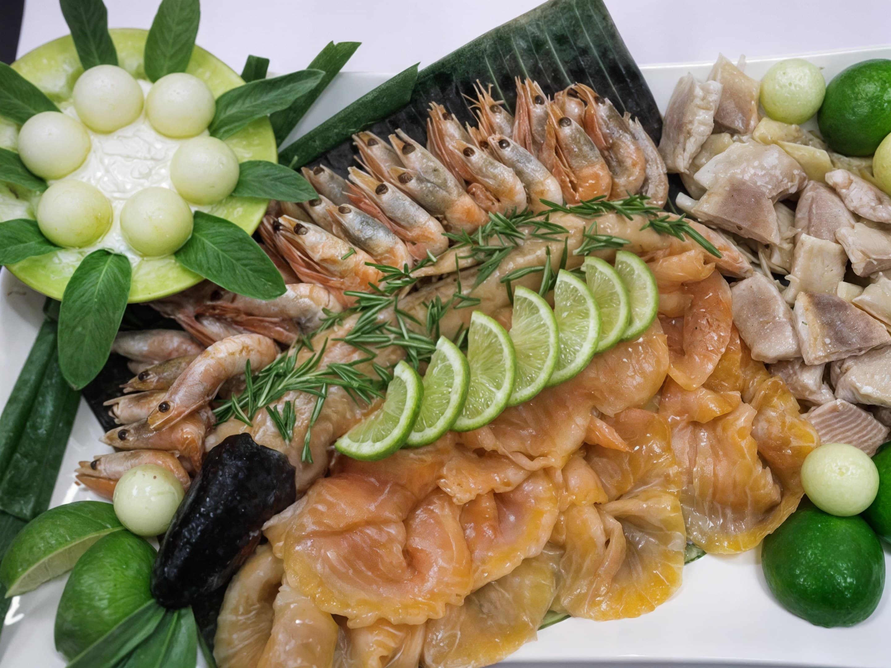 Platte mit Garnelen, Räucherlachs, Forelle, Limettenspalten und Melonenkugeln