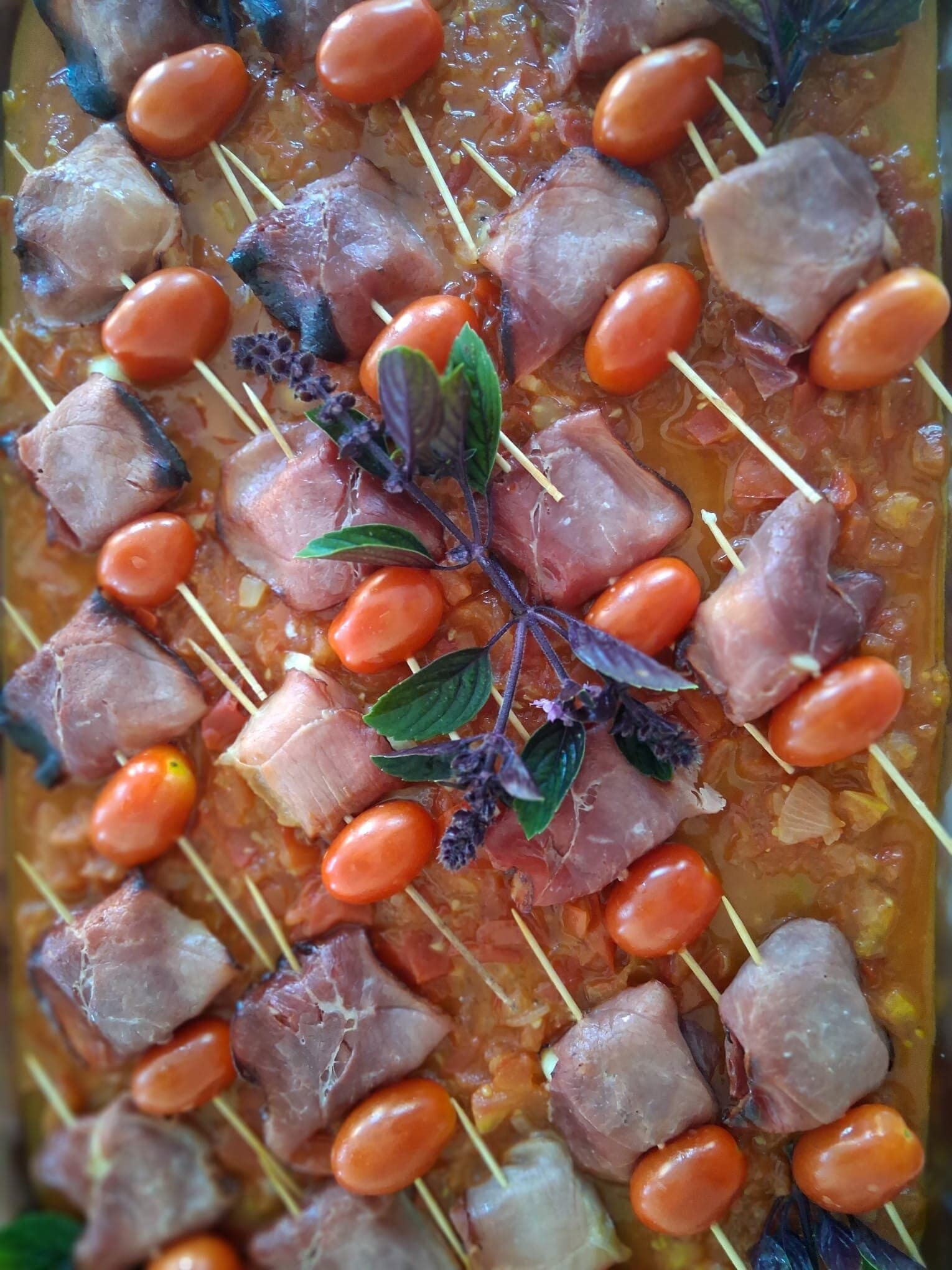 Spiesse mit Schinken und Kirschtomaten in rötlicher Sauce, mit Basilikum