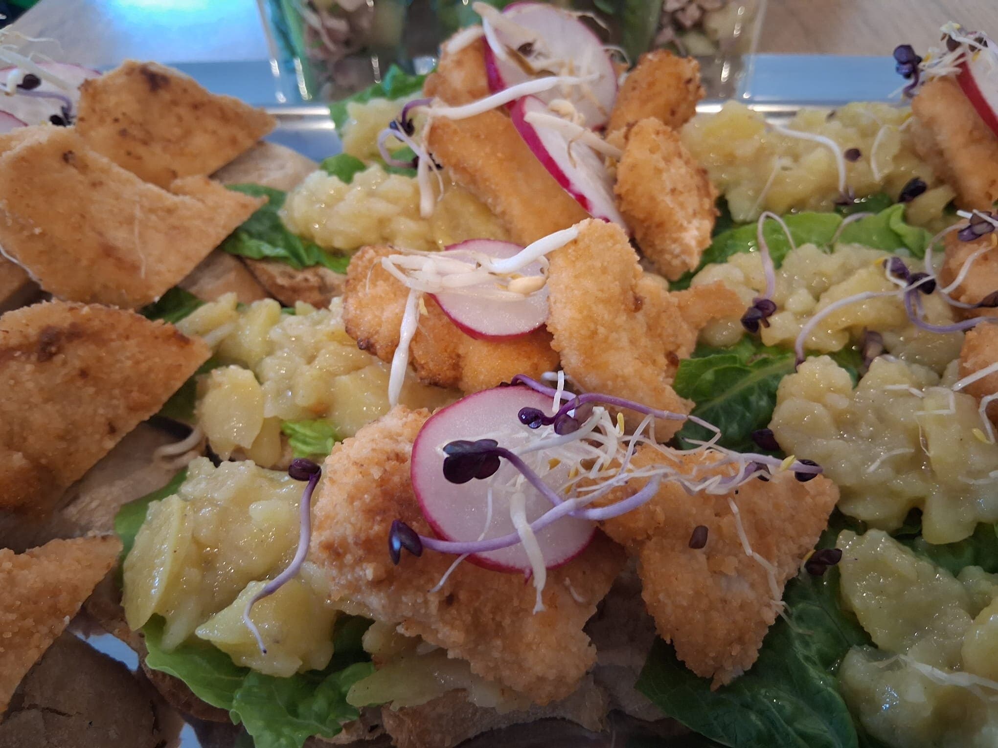 Panierte Fischstücke auf Salat mit Kartoffelsalat und Radieschen