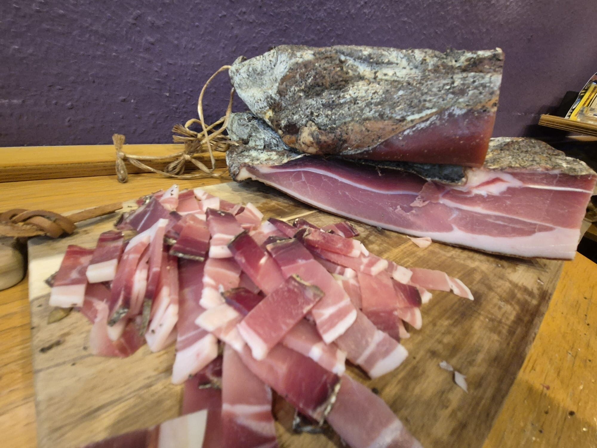 Rohschinken am Stück und geschnitten auf einem Holzbrett