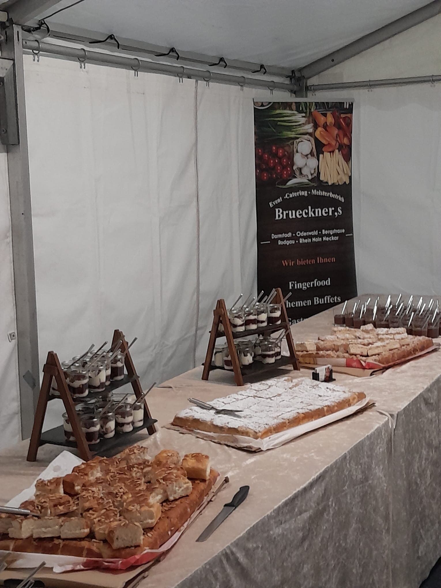 Dessert- und Kuchenbuffet in einem weissen Zelt, dahinter sein Banner